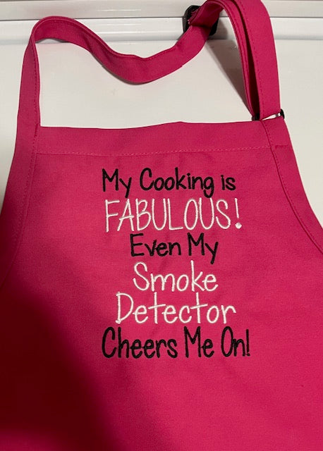 hot pink apron embroidered with My cooking is FABULOUS! Even my smoke detector cheers me on! The embroidery is black and white. 