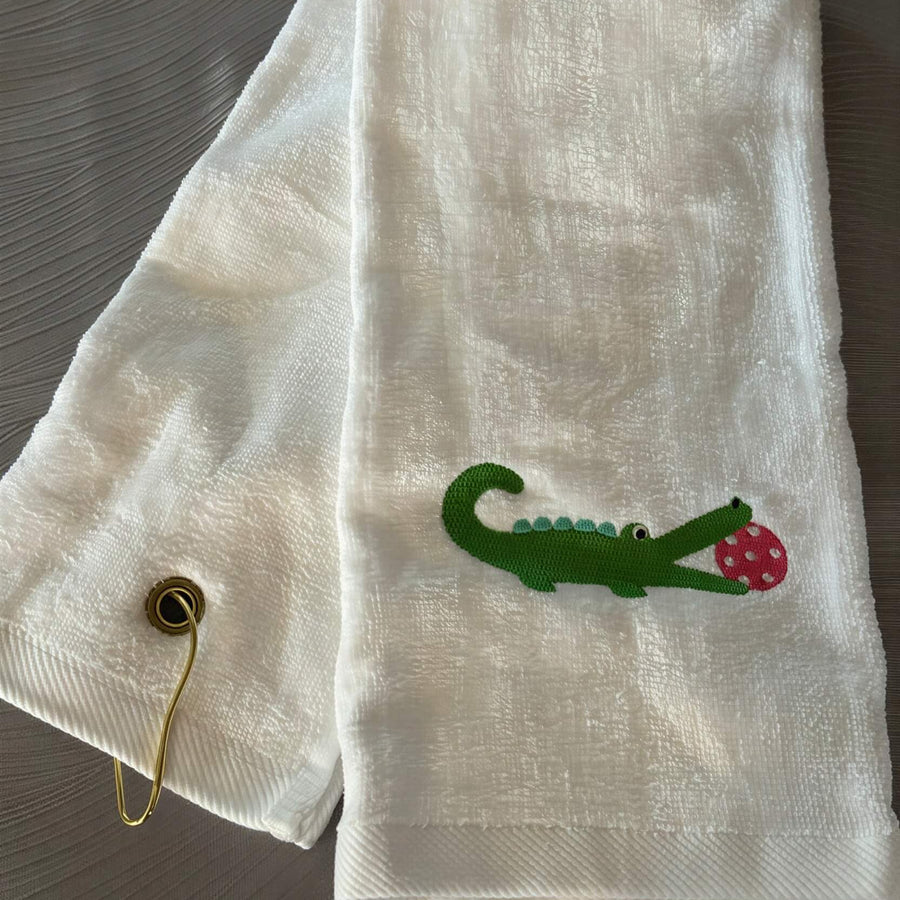 white trifold towel embroidered with a green alligator with a hot pink pickball in it's mouth