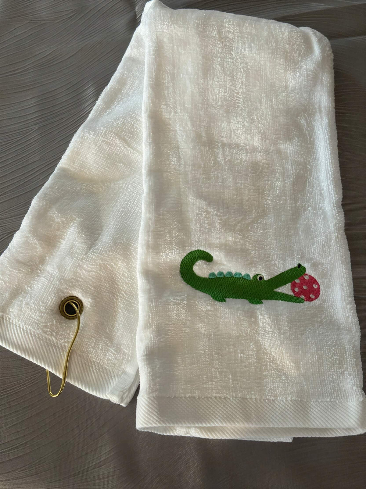 white trifold towel embroidered with a green alligator with a hot pink pickball in it's mouth