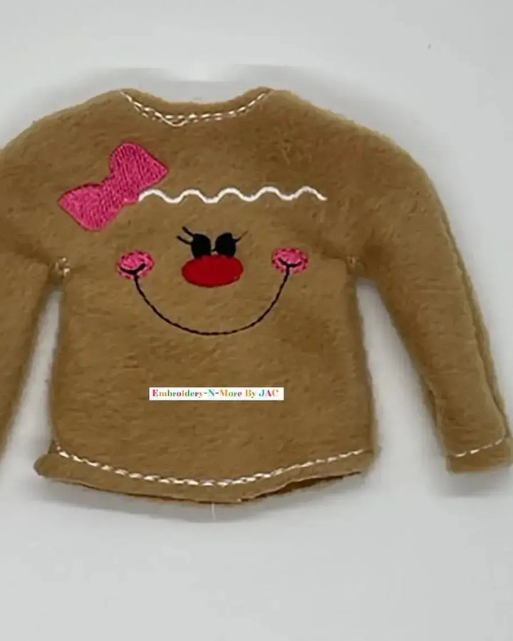 Brown felt doll sweater with embroidered gingerbread face, pink bow, and decorative stitching