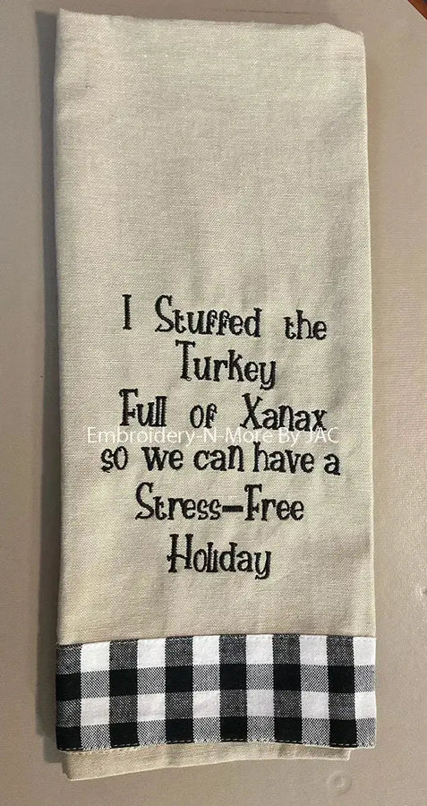 Funny holiday kitchen towel with embroidered joke text and black plaid trim