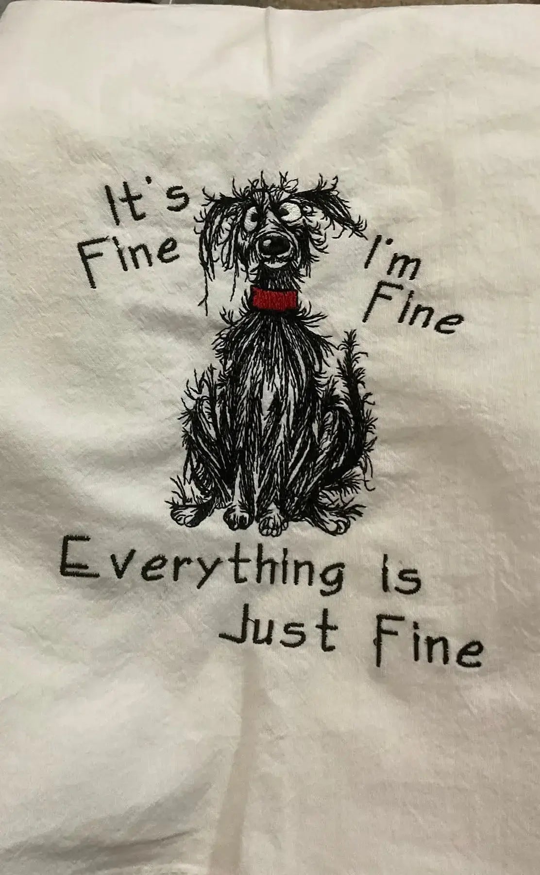 Embroidered kitchen towel with scruffy dog illustration and humorous saying, "It's fine, I'm fine, everything is just fine."