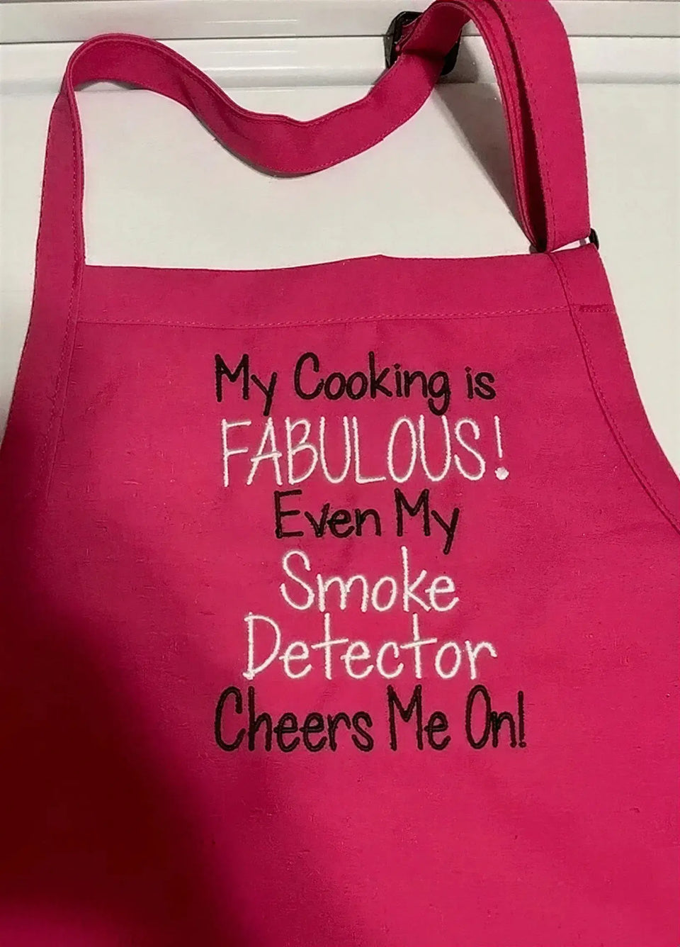 Hot pink apron with humorous white and black embroidered cooking quote on the front