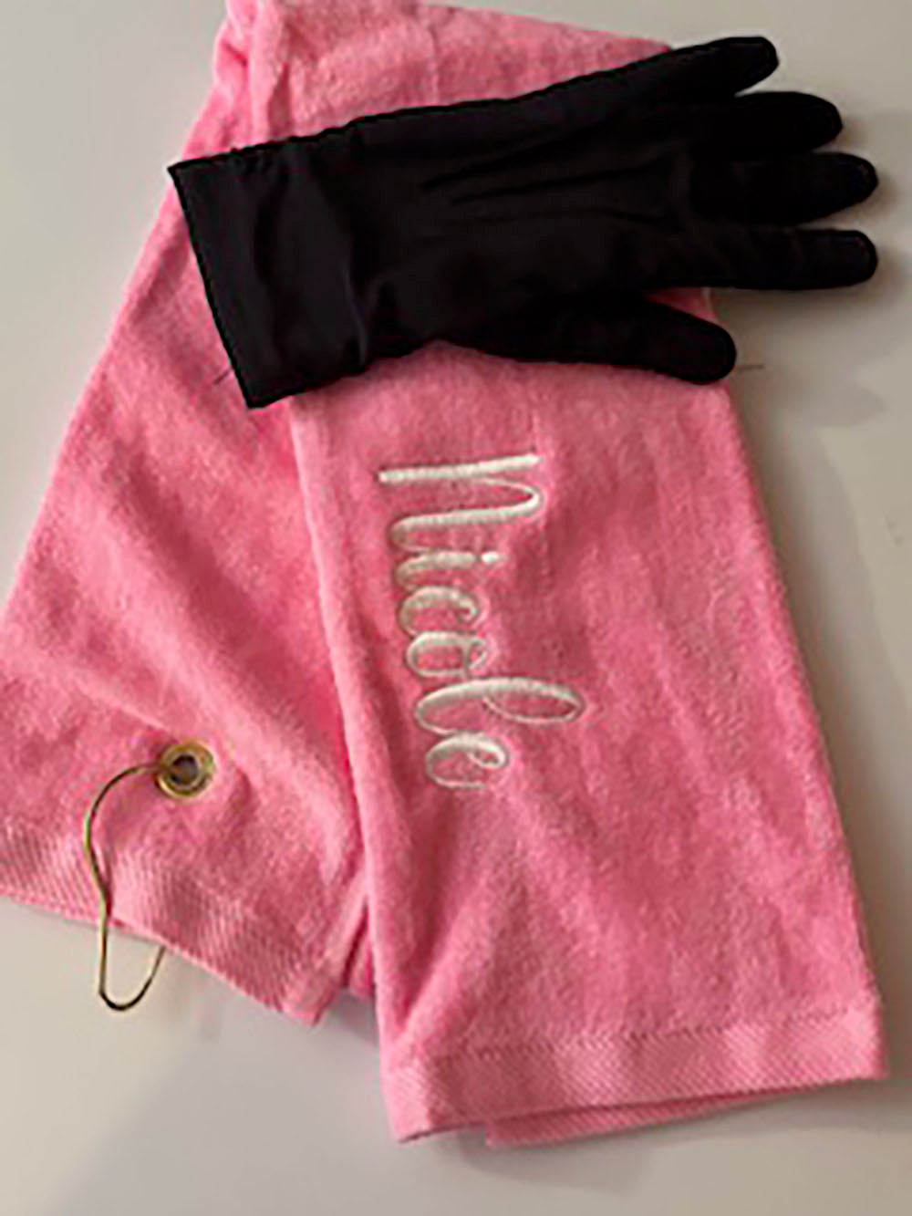 Pink towel with 'Nicole' embroidered on it and black gloves on top, on a light background.