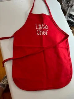 Red children's apron with white embroidered 'Little Chef' text on a white surface