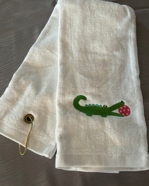 white trifold towel embroidered with a green alligator with a hot pink pickball in it's mouth
