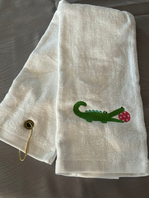 white trifold towel embroidered with a green alligator with a hot pink pickball in it's mouth