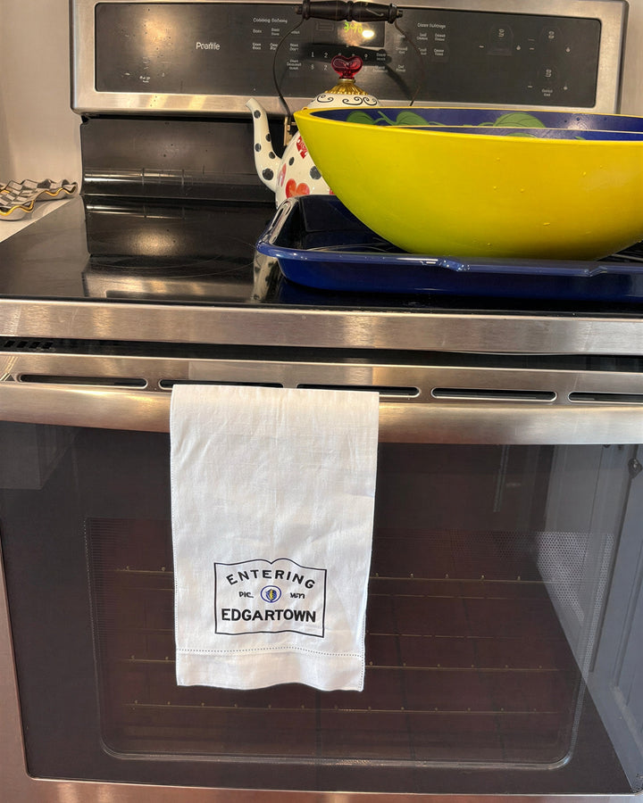 Linen hemsttiched kitchen towel embroidered with Entering Edgartown town sign hanging on a oven handle