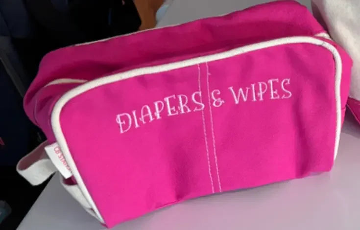 Pink embroidered diapers and wipes pouch for baby essentials on white surface