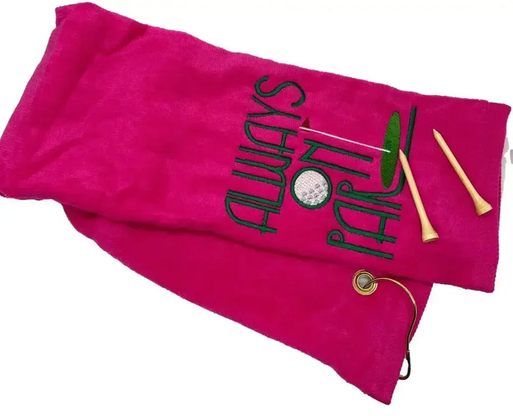 Pink embroidered tri-fold golf towel with Always On Par text, two wooden tees, metal grommet