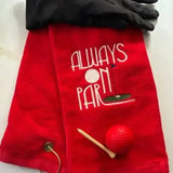 Red embroidered golf towel with 'Always On Par' text, black golf glove, tee, and red golf ball