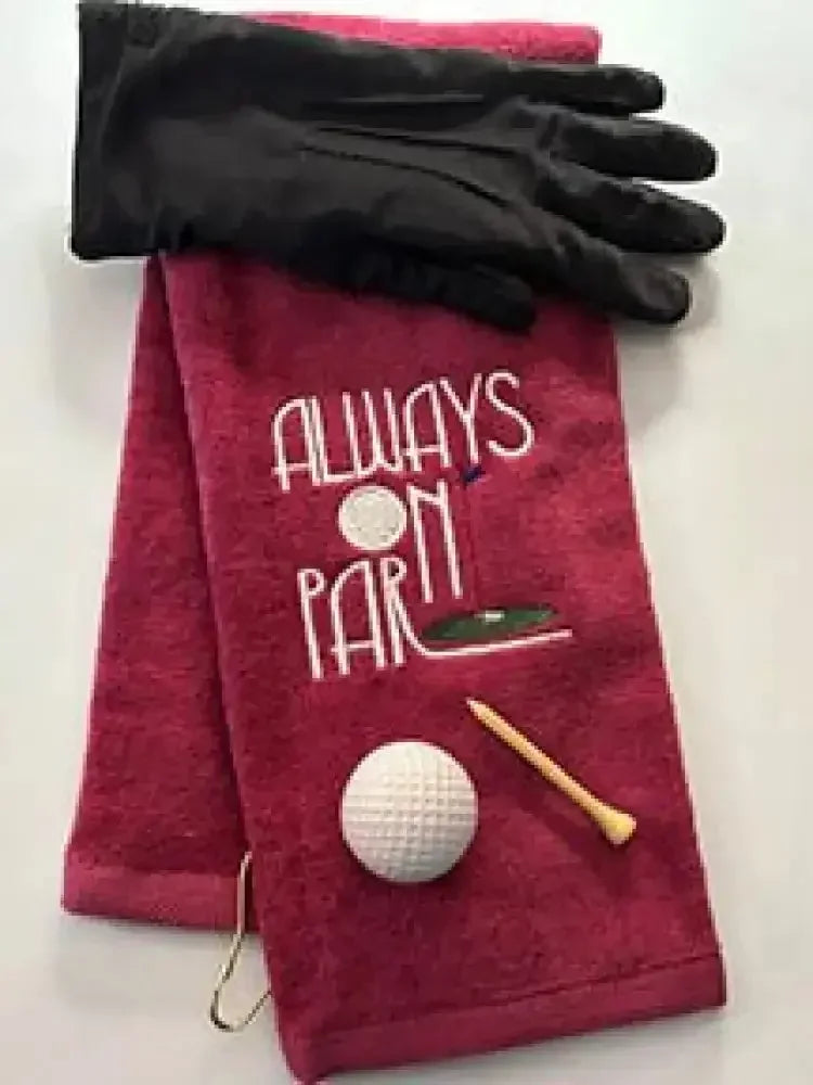 Red embroidered golf towel with 'Always On Par' text, black glove, golf ball, and tee