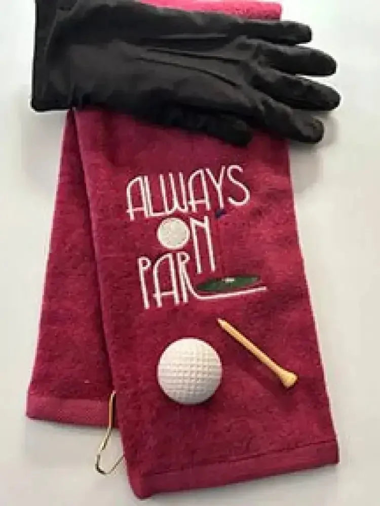 Red embroidered golf towel with 'Always On Par' design, golf glove, ball, and tee