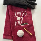 Red embroidered golf towel with 'Always On Par' design, golf glove, ball, and tee