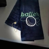 Navy blue embroidered golf towel with 'baller' text and golf ball design, metal grommet