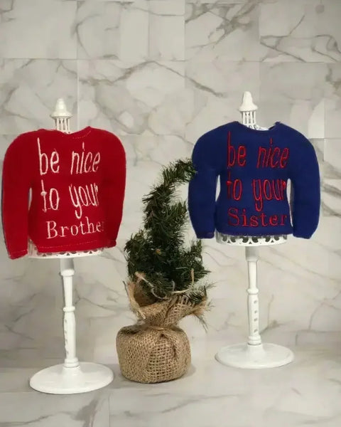 Red and blue embroidered elf sweaters on stands with be nice to your brother and sister text