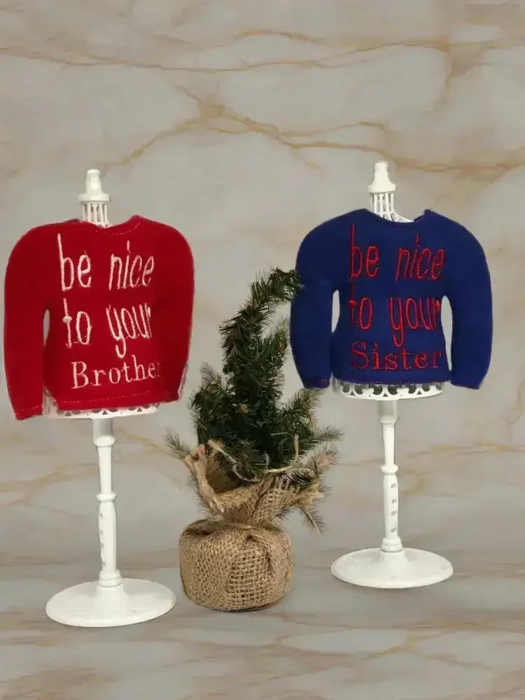 Red and blue embroidered elf sweaters on stands, with a small pine tree between them