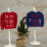 Red and blue embroidered elf sweaters on stands, with a small pine tree between them