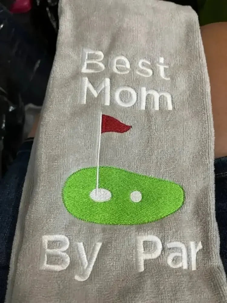 Embroidered golf towel with text 'Best Mom By Par' and green golf green with flag design