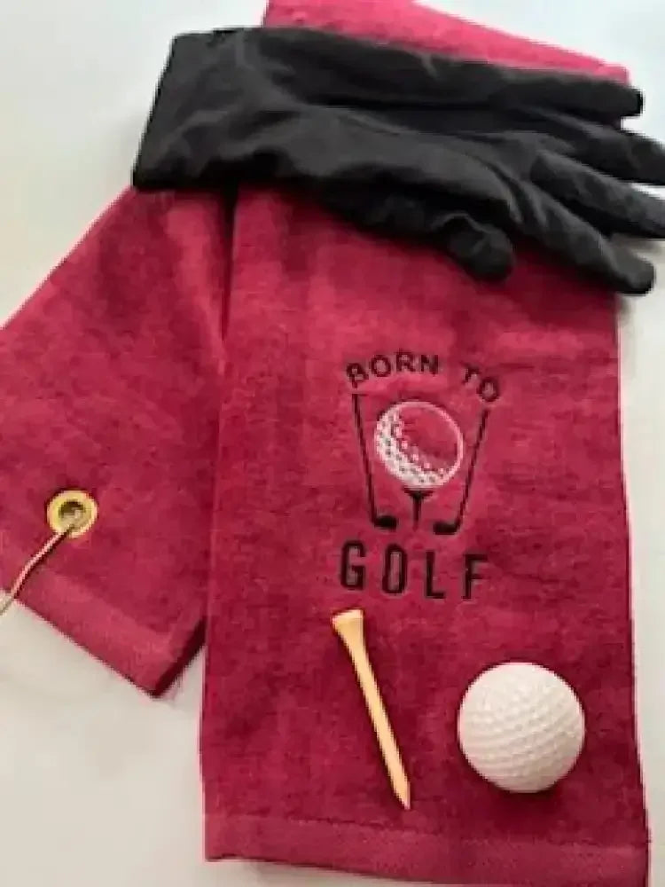 Red embroidered golf towel with 'Born to Golf' text, black glove, golf tee, and golf ball