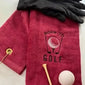 Red embroidered golf towel with 'Born to Golf' text, black glove, golf tee, and golf ball