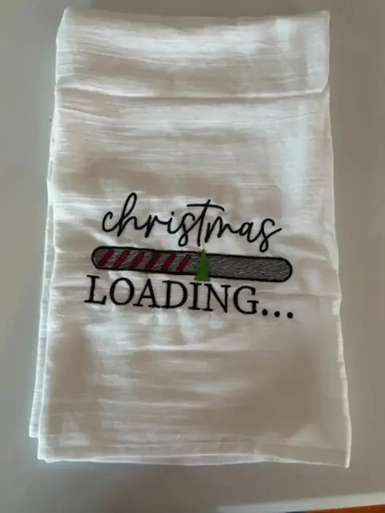 White flour sack kitchen towel with embroidered 'Christmas loading' and festive progress bar design.