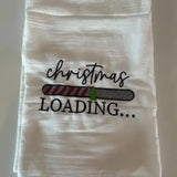 White flour sack kitchen towel with embroidered 'Christmas loading' and festive progress bar design.
