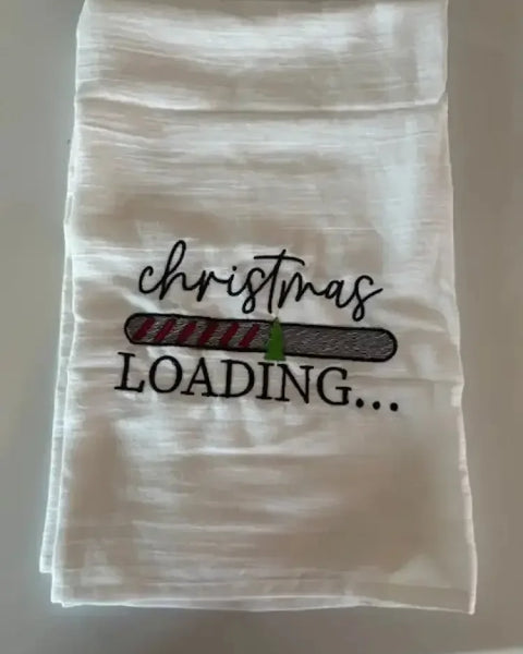 White flour sack kitchen towel with embroidered 'Christmas loading' and festive progress bar design.
