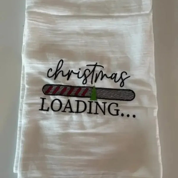 White flour sack kitchen towel with embroidered 'Christmas loading' and festive progress bar design.