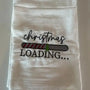 White flour sack kitchen towel with embroidered 'Christmas loading' and festive progress bar design.