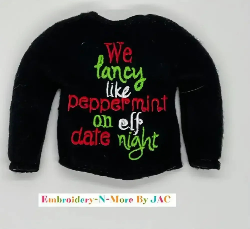 Black sweater with embroidered festive text in red, green, and white, holiday themed.