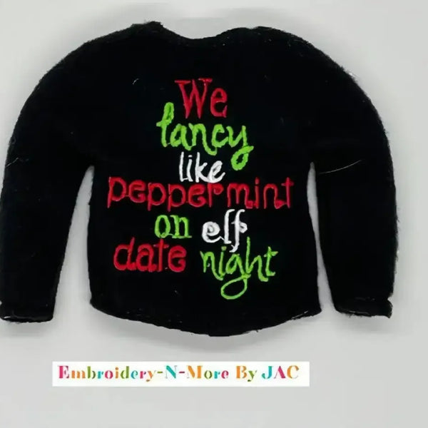 Black sweater with embroidered festive text in red, green, and white, holiday themed.