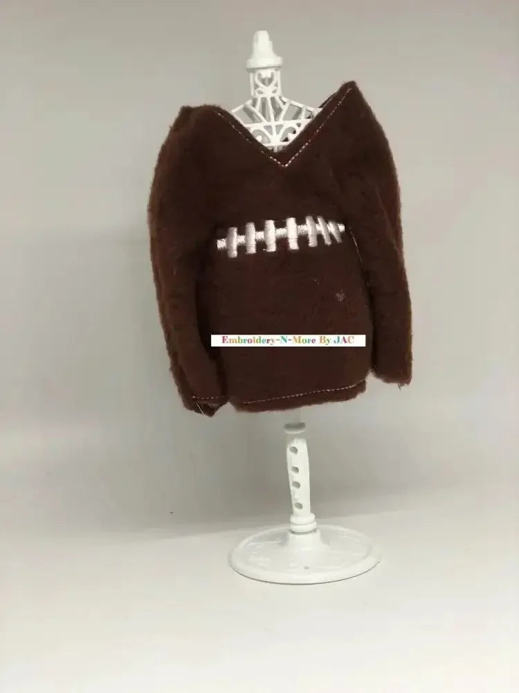 Brown elf sweater styled like a football with white embroidered stitching on display stand