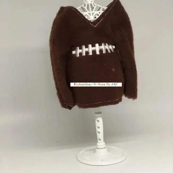 Brown elf sweater styled like a football with white embroidered stitching on display stand