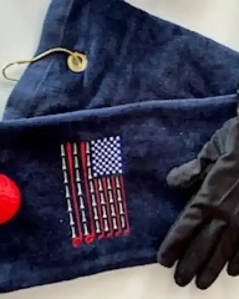 Navy golf towel with embroidered USA flag made from golf tees, red golf ball, and black glove