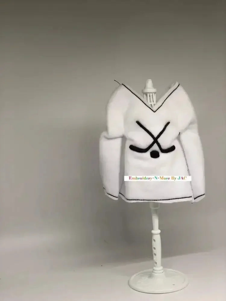 White hockey-themed elf sweater with crossed hockey sticks, displayed on a mannequin stand.
