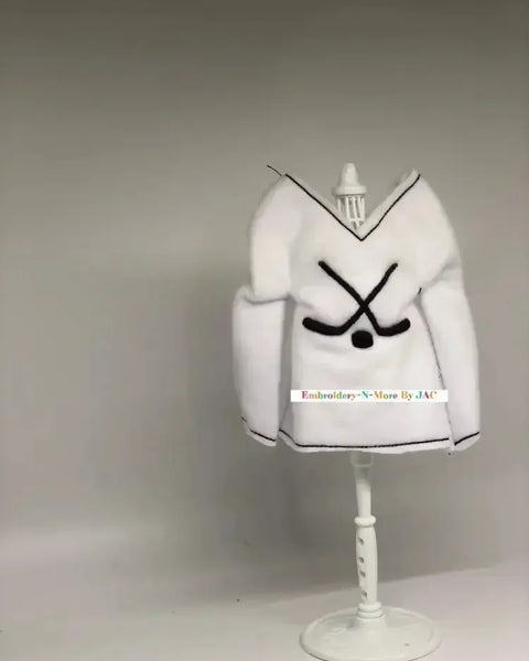 White hockey-themed elf sweater with crossed hockey sticks, displayed on a mannequin stand.