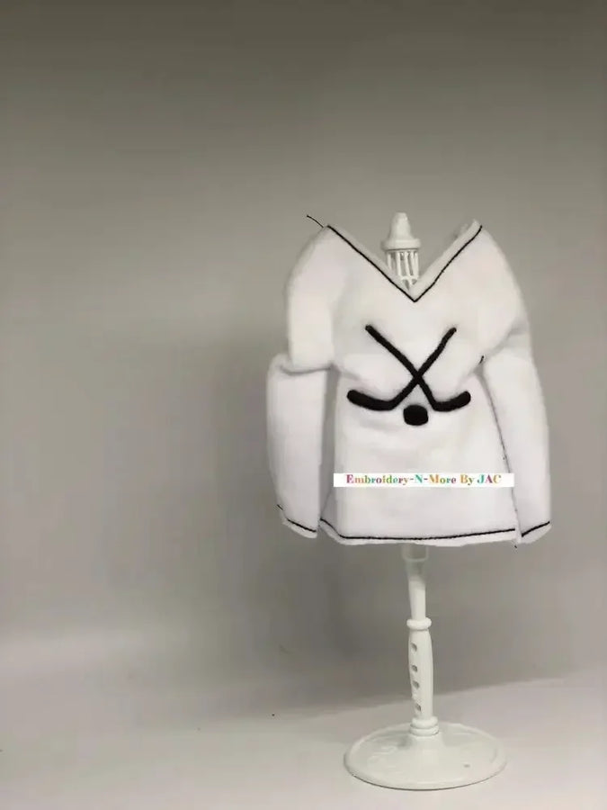 White hockey-themed elf sweater with crossed hockey sticks, displayed on a mannequin stand.