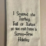 Beige embroidered hand towel with humorous holiday saying and black plaid trim.