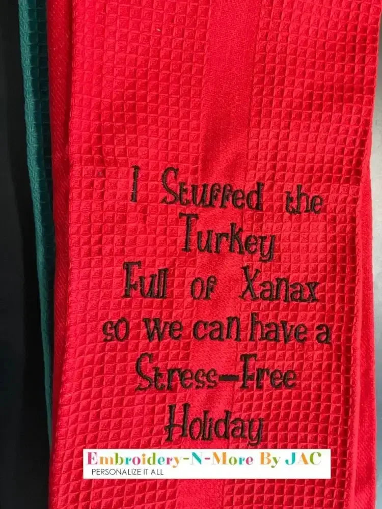 Red embroidered kitchen towel with humorous holiday text, waffle texture, black stitching.