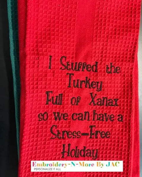 Red embroidered kitchen towel with humorous holiday text, waffle texture, black stitching.