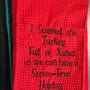 Red embroidered kitchen towel with humorous holiday text, waffle texture, black stitching.