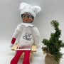 Elf doll wearing white chef costume and hat, sitting by a small decorative Christmas tree