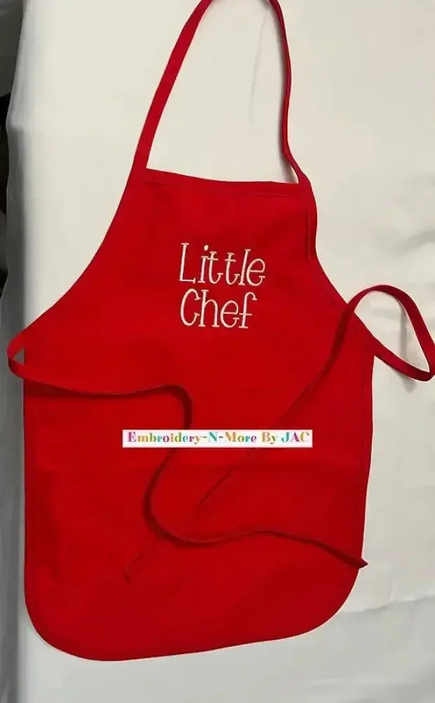 Red children's apron with 'Little Chef' embroidered on the front, displayed on a white surface.