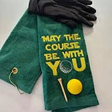 Green embroidered golf towel with 'May the Course Be With You' text, golf glove, ball, and tee.