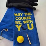 Blue embroidered golf towel with 'May the course be with you' text, golf glove, ball, and tee