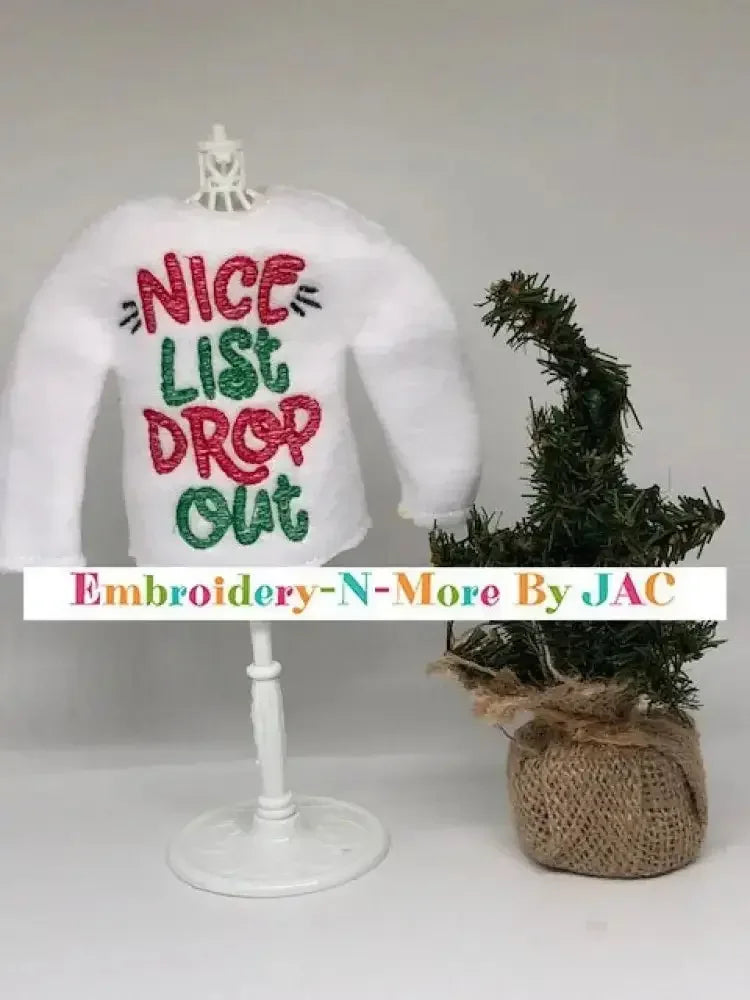 White elf sweater with 'Nice List Drop Out' embroidered in red and green, next to mini Christmas tree.