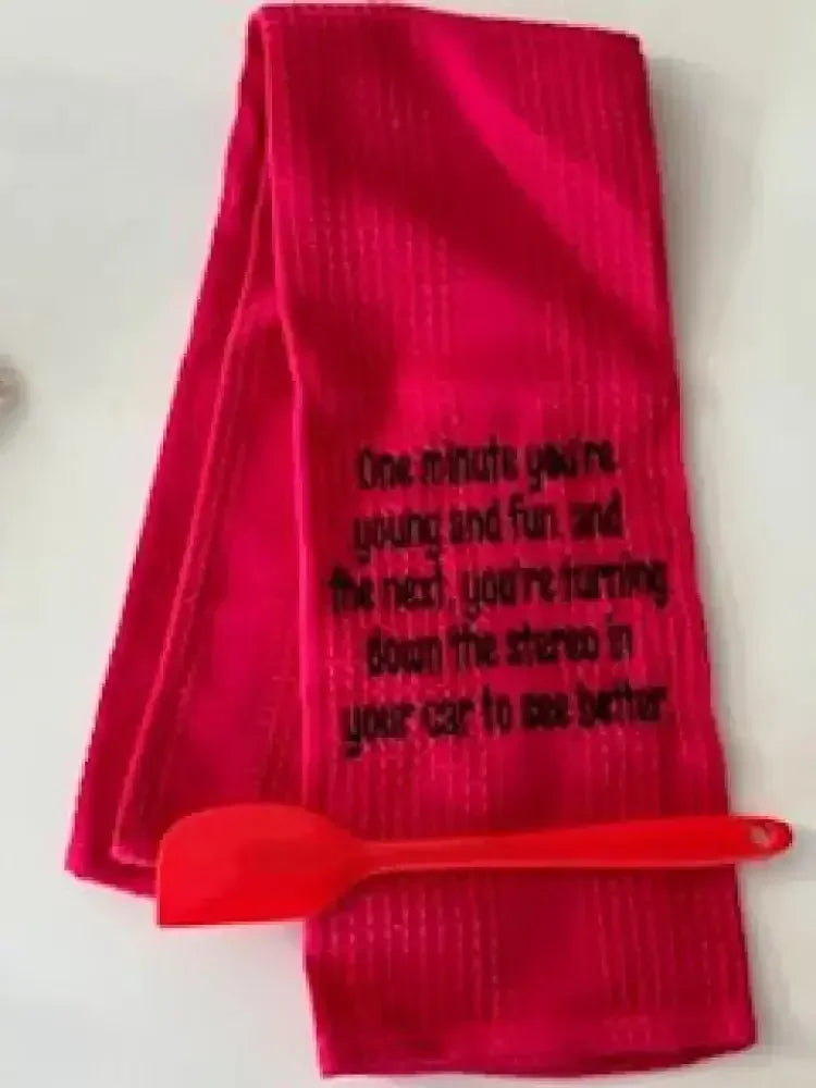Red flour sack kitchen towel with humorous embroidered quote and red spatula on white surface