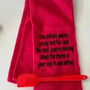 Red flour sack kitchen towel with humorous embroidered quote and red spatula on white surface