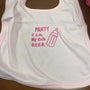 Pink embroidered baby bib with bottle and party-themed text on wooden table